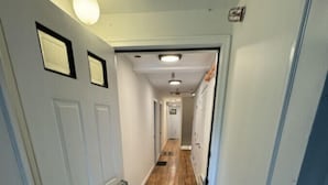 A narrow hallway with a door on the left, a light fixture above, and a doormat at the entrance. - The Stern at Soundview · Beach+Ocean+Sunrise (Old Lyme)