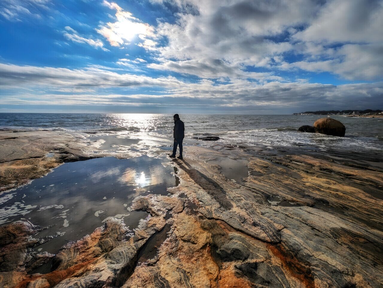 Una persona de pie sobre una costa rocosa, con vista al océano y un cielo nublado.