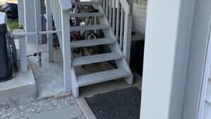 Un escalier menant à une véranda couverte, agrémentée d’un portail en métal et d’un support à vélos.