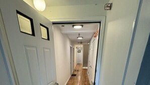 Un couloir étroit avec une porte sur la gauche, un luminaire au-dessus et un paillasson à l’entrée.