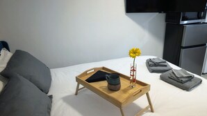 Un lit bien fait, avec un plateau en bois sur lequel se trouvent une tasse et un vase rempli de fleurs.