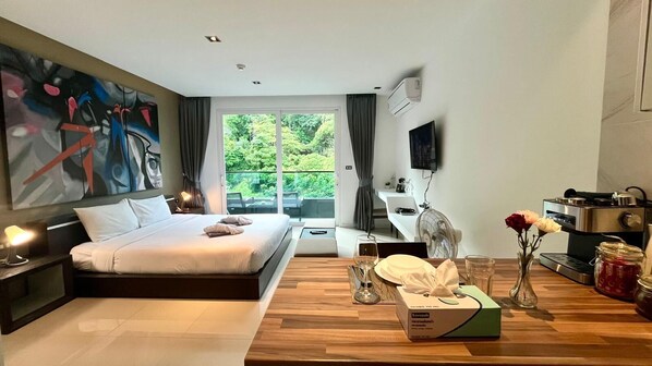Habitación de hotel moderna con una cama grande, una mesa de comedor, un televisor y vistas a zonas verdes.
