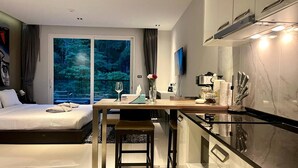 Et moderne hotelværelse med seng, skrivebord og udsigt til en skov gennem store vinduer.