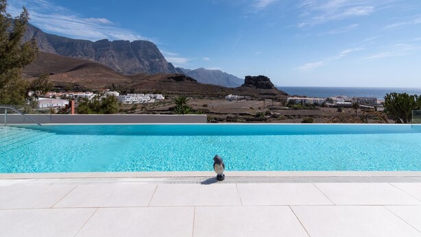 A swimming pool with a clear view of mountains and the sea in the background.