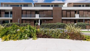 A modern multi-story building with a flat roof, large windows, and a landscaped garden area in front.