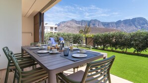 A dining table set for four with plates, cups, and a coffee pot, overlooking a mountainous landscape.