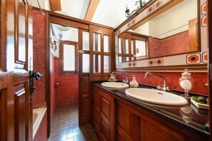 Bathroom features two sinks, a large mirror, and a wooden vanity with drawers.