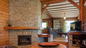 A cozy cabin interior with a stone fireplace, wooden beams, a television, and a dining area. - Rendeux Valley View Retreat (Rendeux-Beffe)