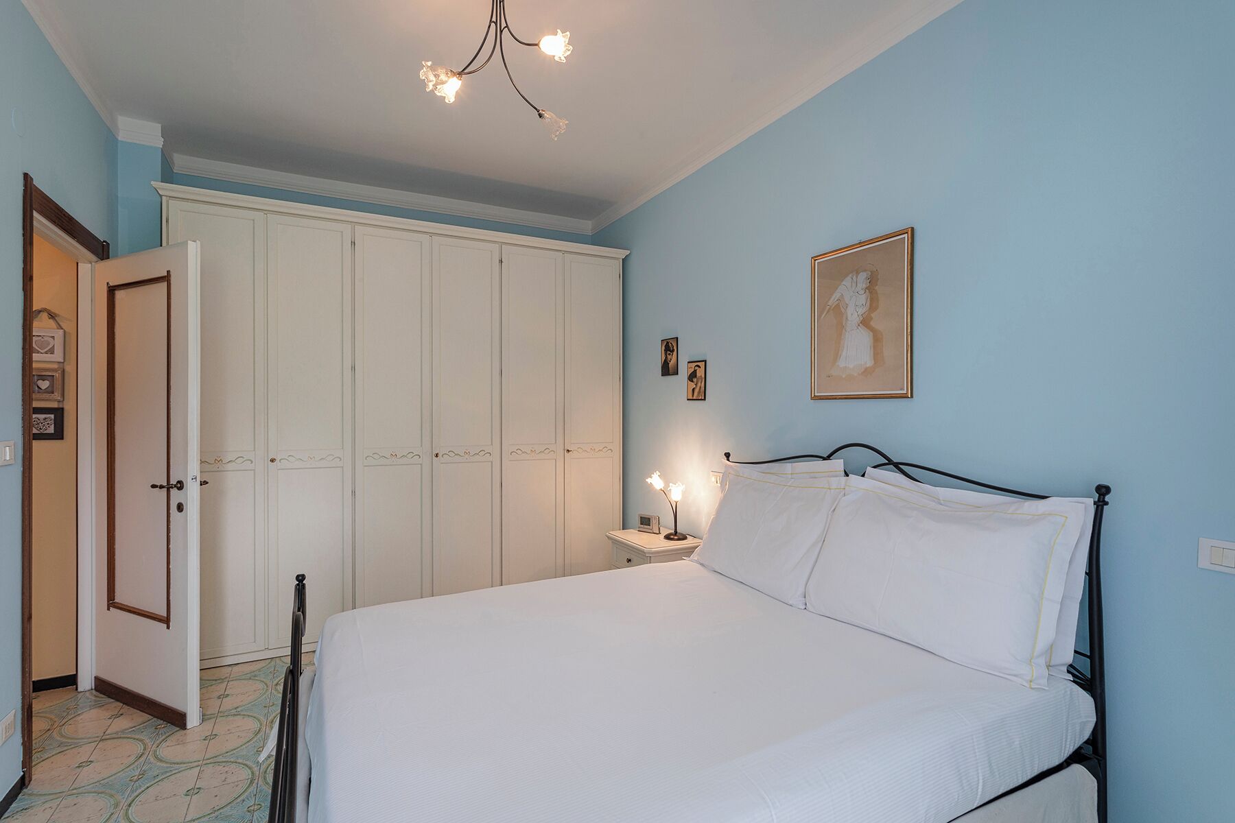 A bedroom with a bed, a nightstand, a white wardrobe, and a chandelier.