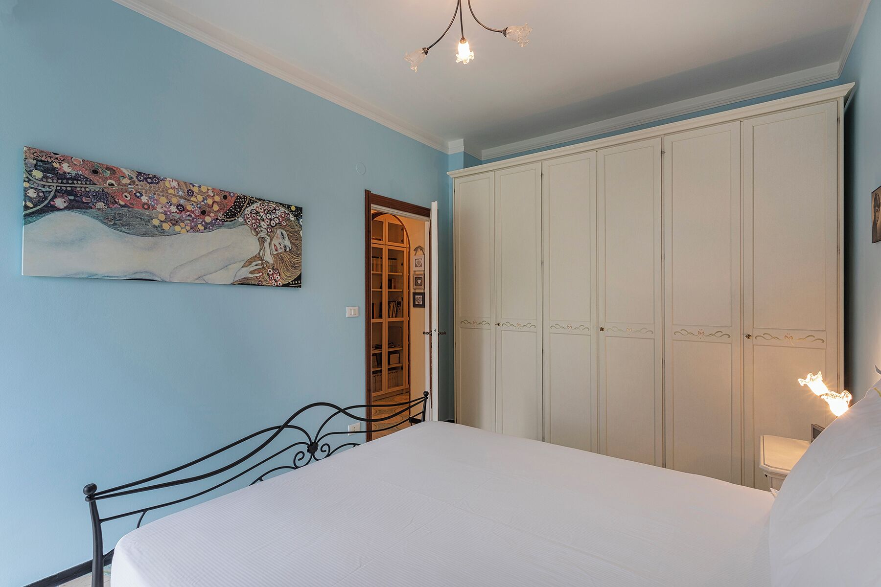 A bedroom with a bed, a wardrobe, a painting, and a chandelier.