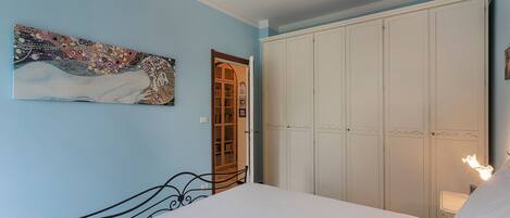 A bedroom with a bed, a wardrobe, a painting, and a chandelier.