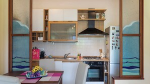 Een compacte keuken met een fornuis, spoelbak en koelkast. Er is een eettafel met stoelen en een vaas zonnebloemen.
