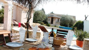 An outdoor dining area with wooden tables, white plates, wine glasses, and a bottle of wine. - Villa in Languedoc with Pool near Historic Cities (Rousson)