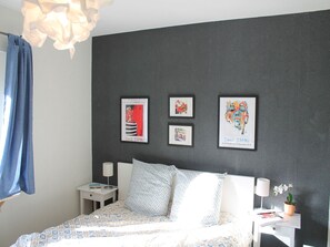 Un dormitorio con una cama, una mesita de noche, una lámpara y tres cuadros enmarcados en la pared.