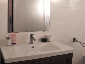 Un baño con un lavamanos blanco, un espejo y un perchero para toallas.