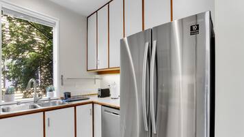 Una cocina moderna con refrigerador de acero inoxidable, gabinetes de madera y ventana con vista a la vegetación.
