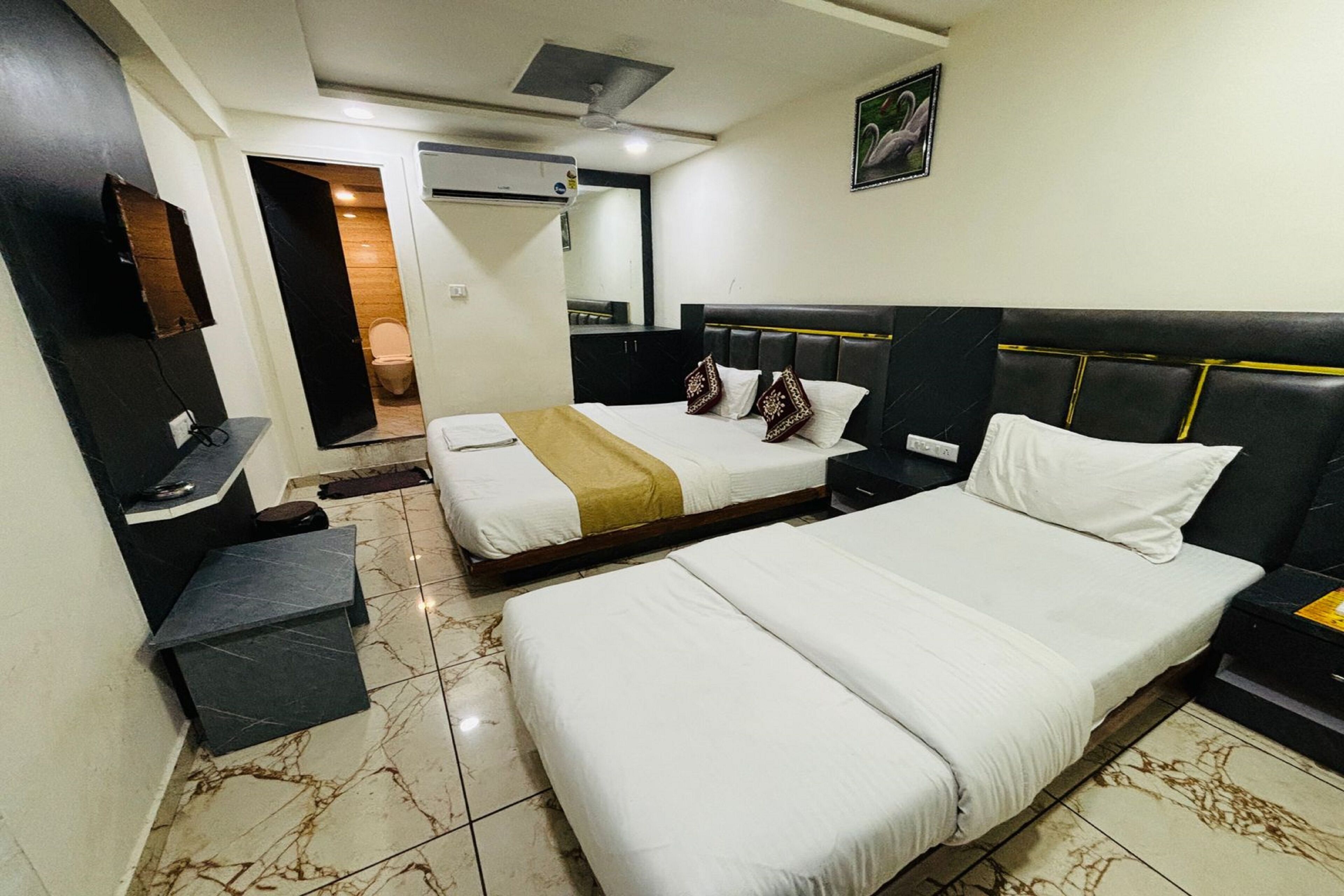 A hotel room with two beds, a desk, a chair, a mirror, and an air conditioning unit.