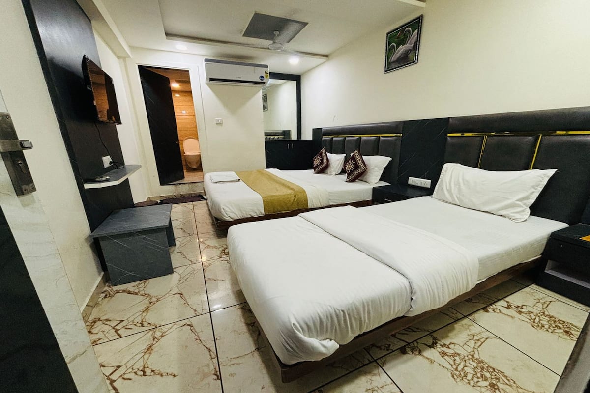 Una habitación de hotel con una cama grande, una cama más pequeña, un televisor montado en la pared y un equipo de aire acondicionado.