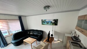 A modern living room with a black leather sofa, a wooden coffee table, and a beige armchair. A painting of a tropical beach hangs on the wall.