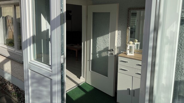 A room with a white door, a small table with a chair, a mirror, and a cabinet.