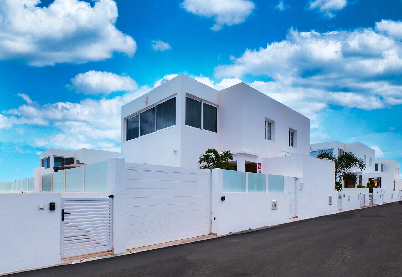 A modern white building with a flat roof, large windows, and a gated entrance.
