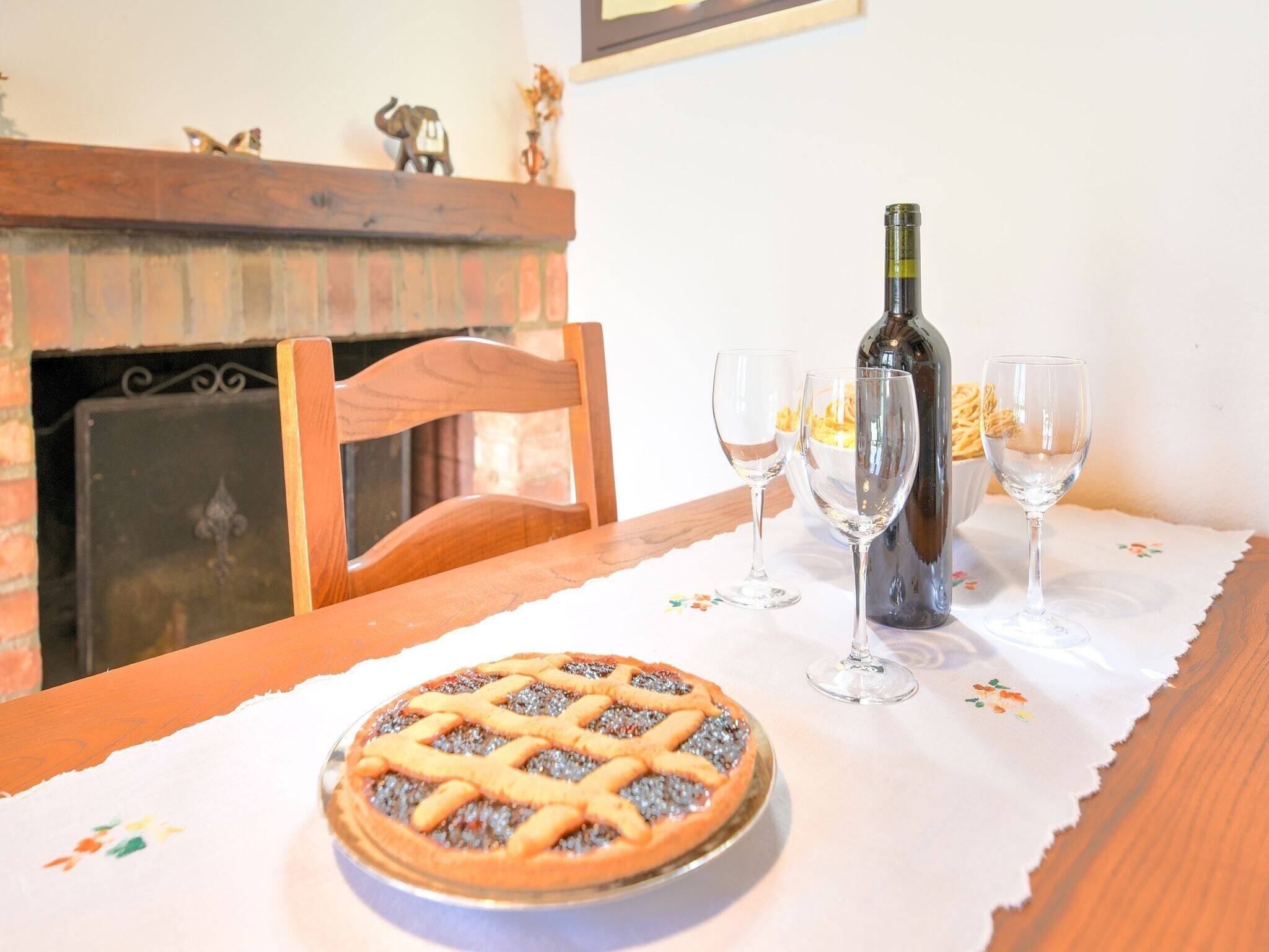A dining table with a pie, two wine glasses, and a bottle of wine.