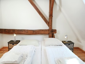 A room with two beds, wooden beams, white walls, and two bedside tables with lamps.