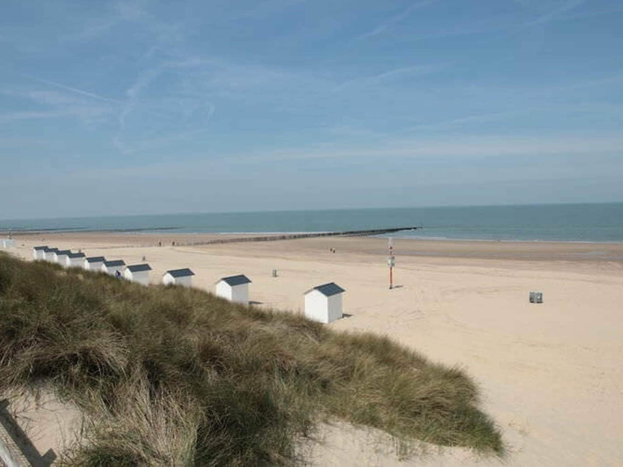A sandy beach with white beach huts and a clear sky.