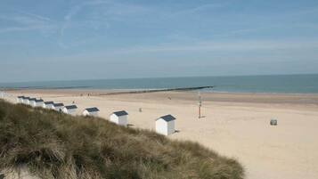 A sandy beach with white beach huts and a clear sky.