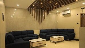 Un área de espera moderna con dos sofás oscuros, una mesa de centro de madera clara y un aire acondicionado de pared.
