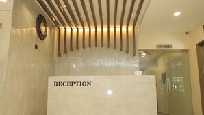 Un área de recepción con mostrador de mármol que dice "RECEPTION", listones de madera en el techo y una puerta de cristal al fondo.