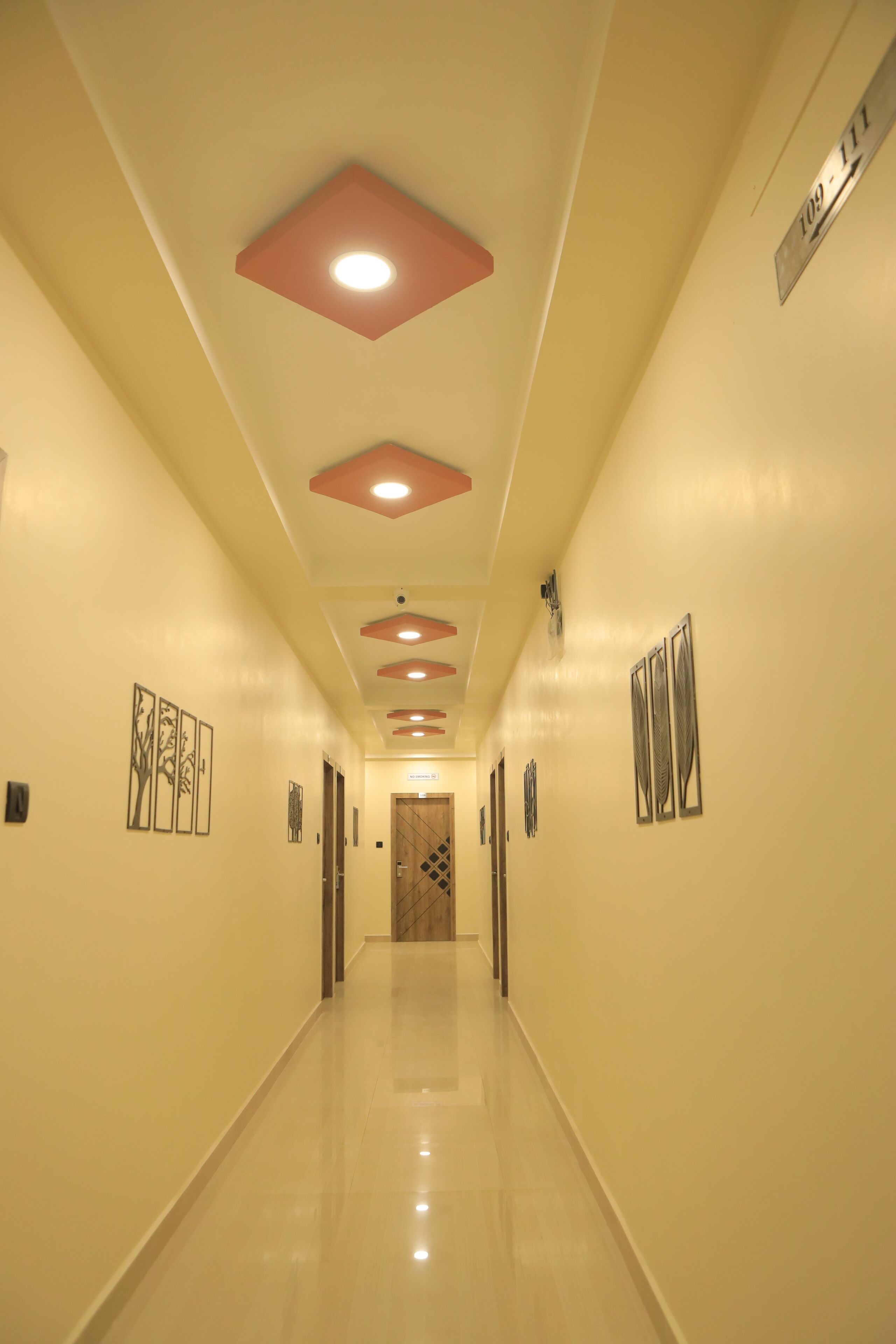 A hallway with a polished floor, recessed lighting, and artwork on the walls.