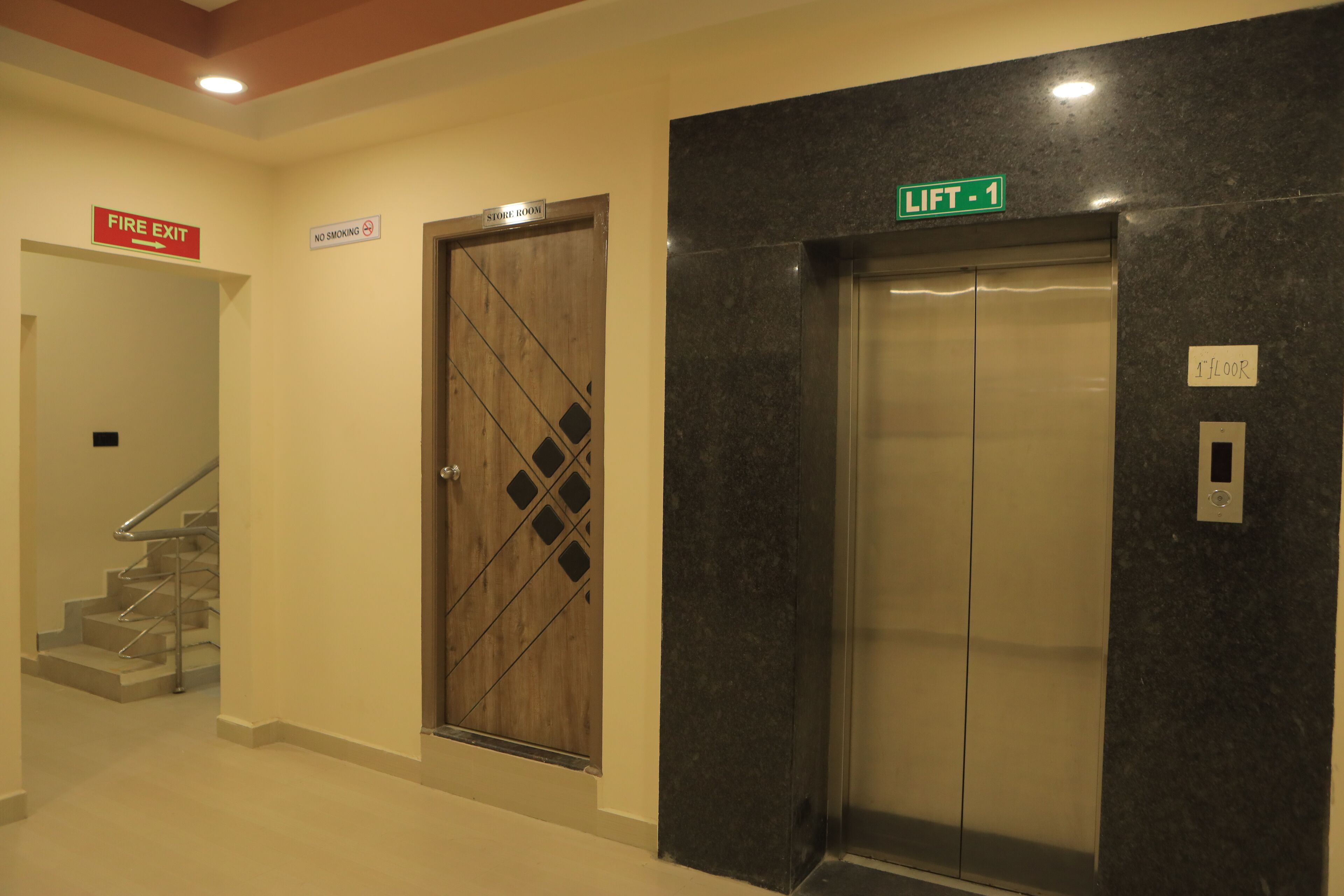 A hotel lobby with a fire exit sign, a no smoking sign, a store room sign, and an elevator with a lift indicator.
