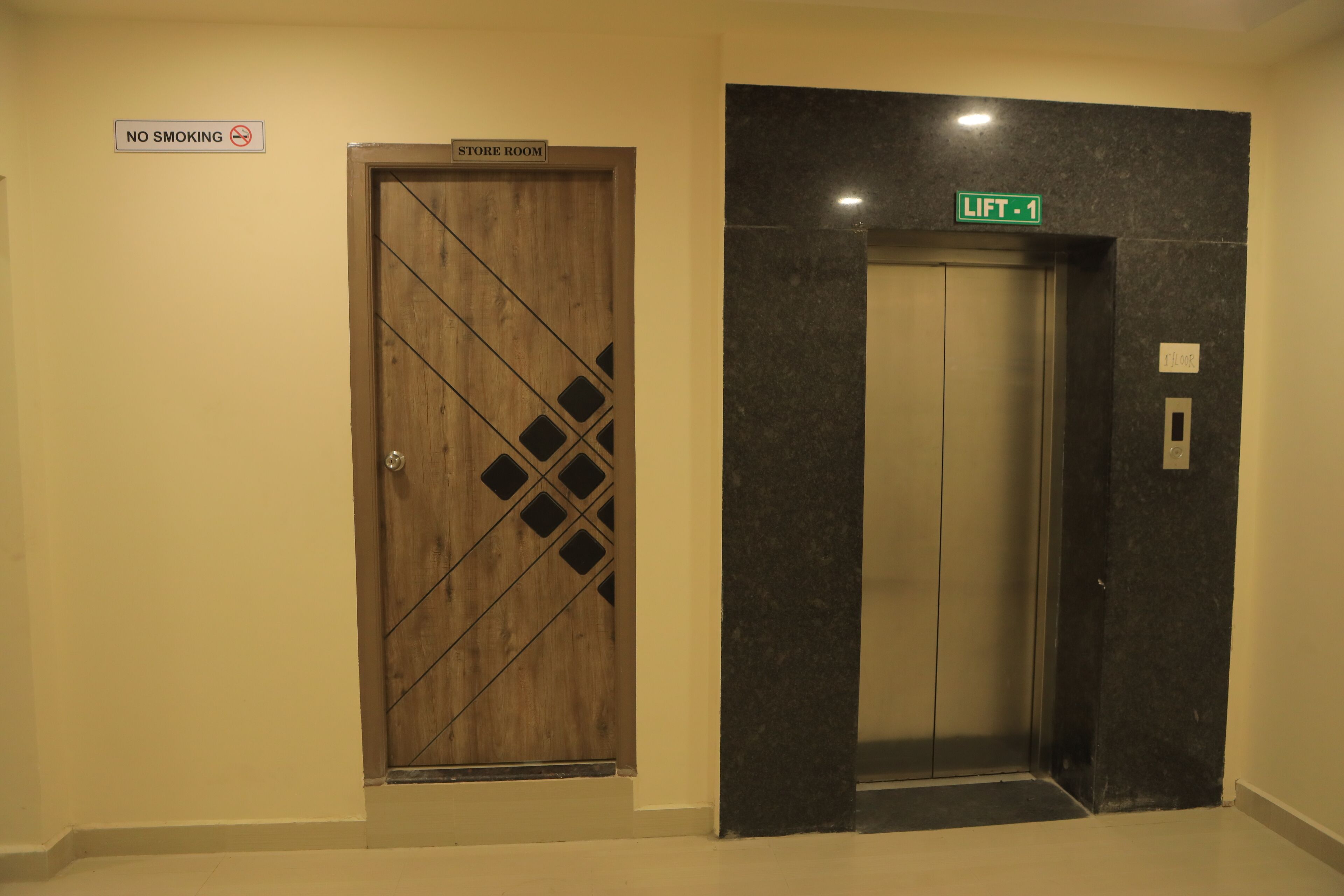 A hotel elevator with a marble wall and a wooden door with a diamond pattern. There is a 'NO SMOKING' sign above the door and a 'LIFT 1' sign above the elevator.
