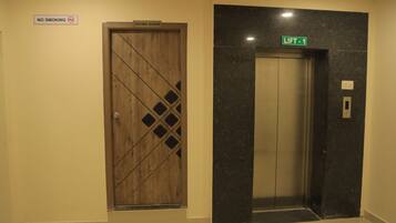A hotel elevator with a marble wall and a wooden door with a diamond pattern. There is a 'NO SMOKING' sign above the door and a 'LIFT 1' sign above the elevator.