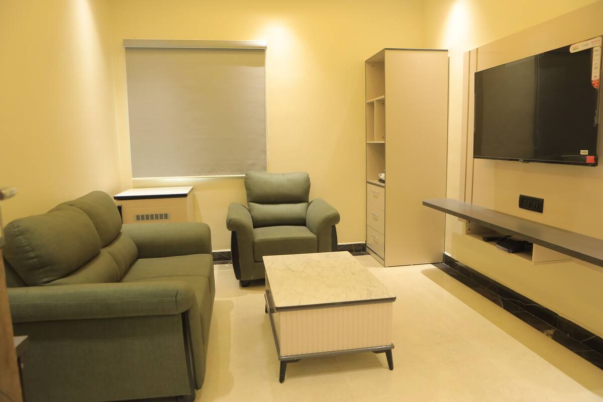 Una sala de estar moderna con sofá, sillón, mesa de centro, televisor y estanterías empotradas.