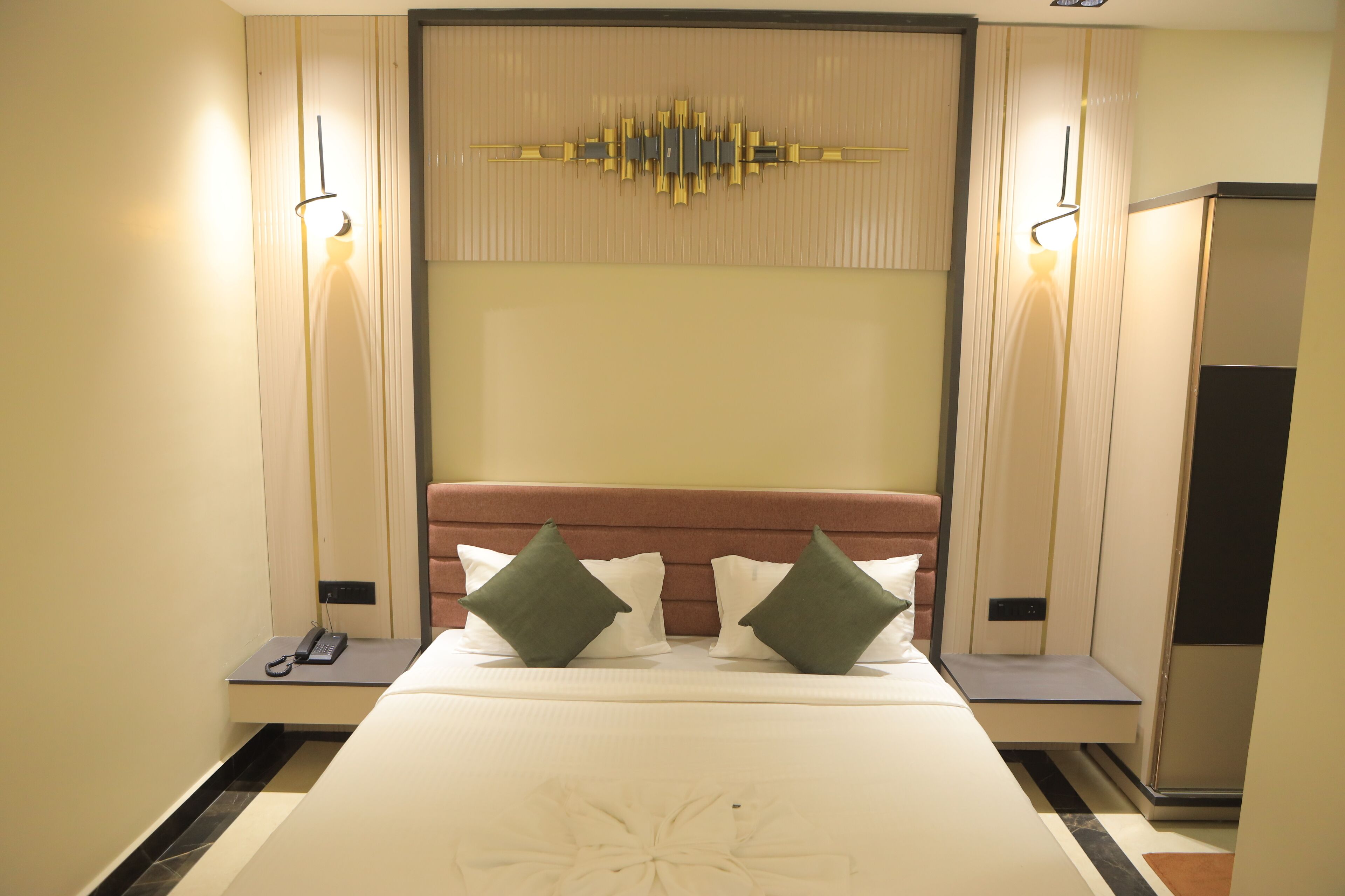 A hotel room with a bed, bedside tables, a wall-mounted light, and a decorative panel above the bed.