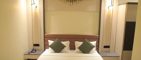 A hotel room with a bed, bedside tables, a wall-mounted light, and a decorative panel above the bed.