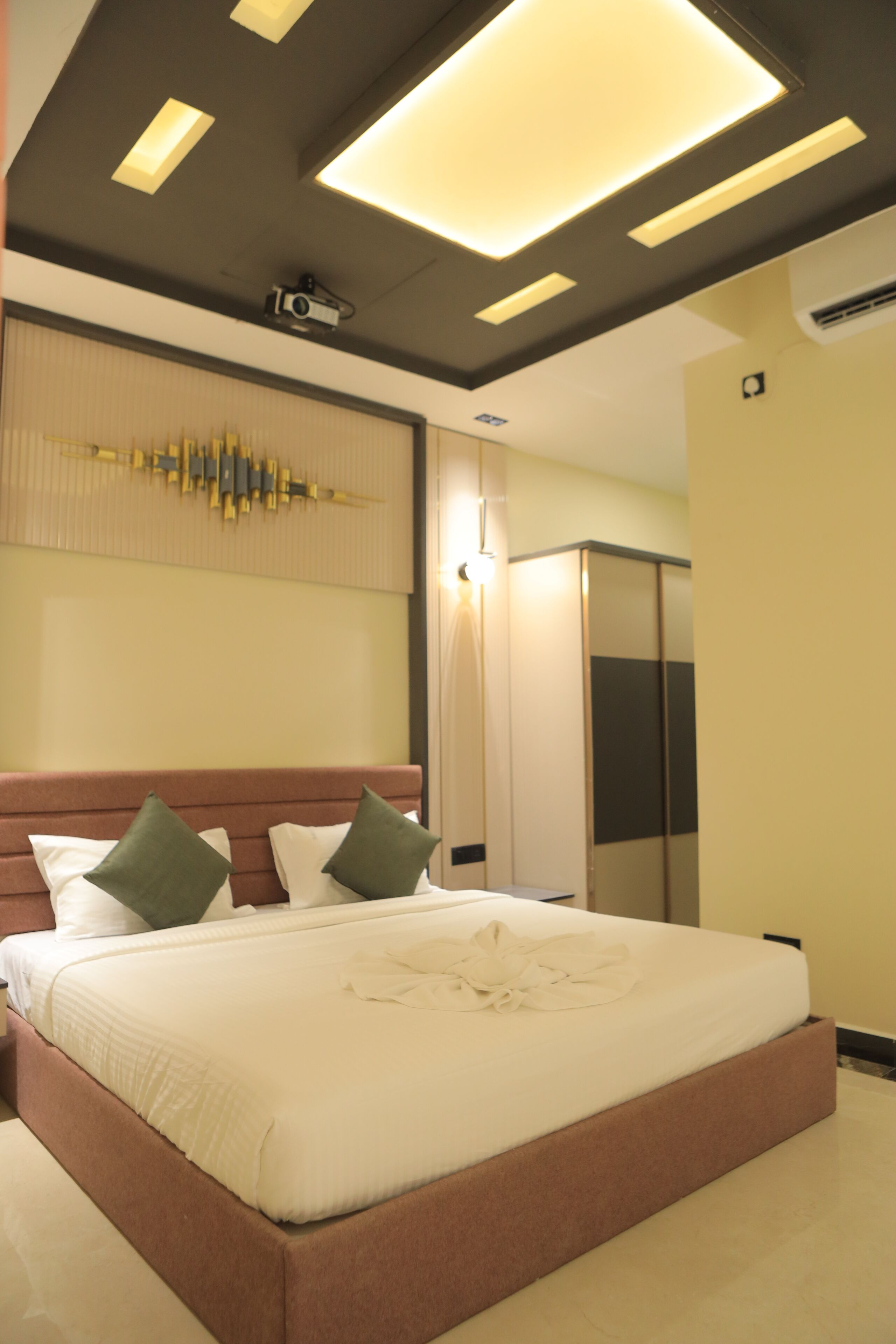 A modern hotel room with a large bed, a ceiling projector, and a wardrobe.