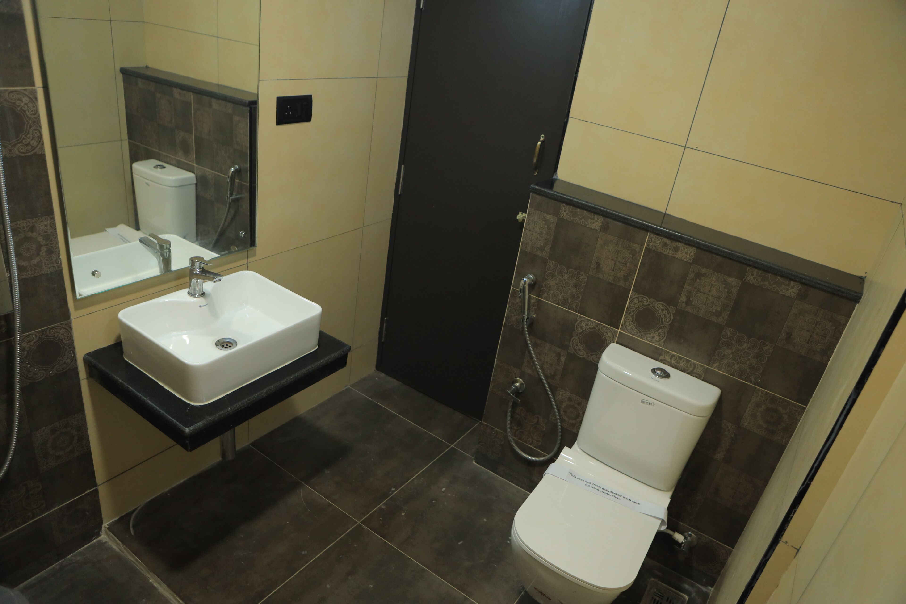 A bathroom with a white sink, a mirror, a black door, and a toilet.