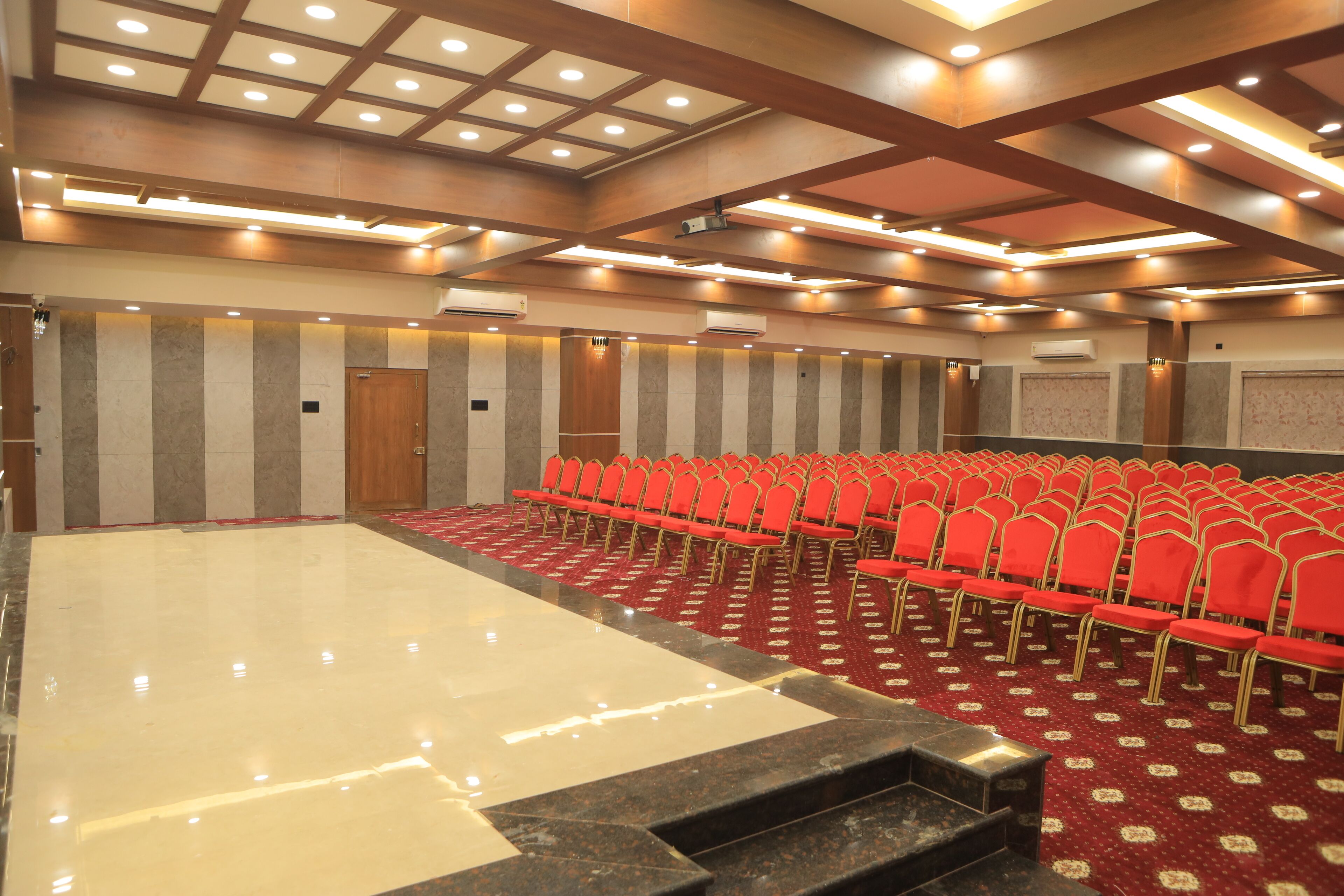 Un salón de conferencias con hileras de sillas rojas, suelo de mármol y una zona para el escenario.