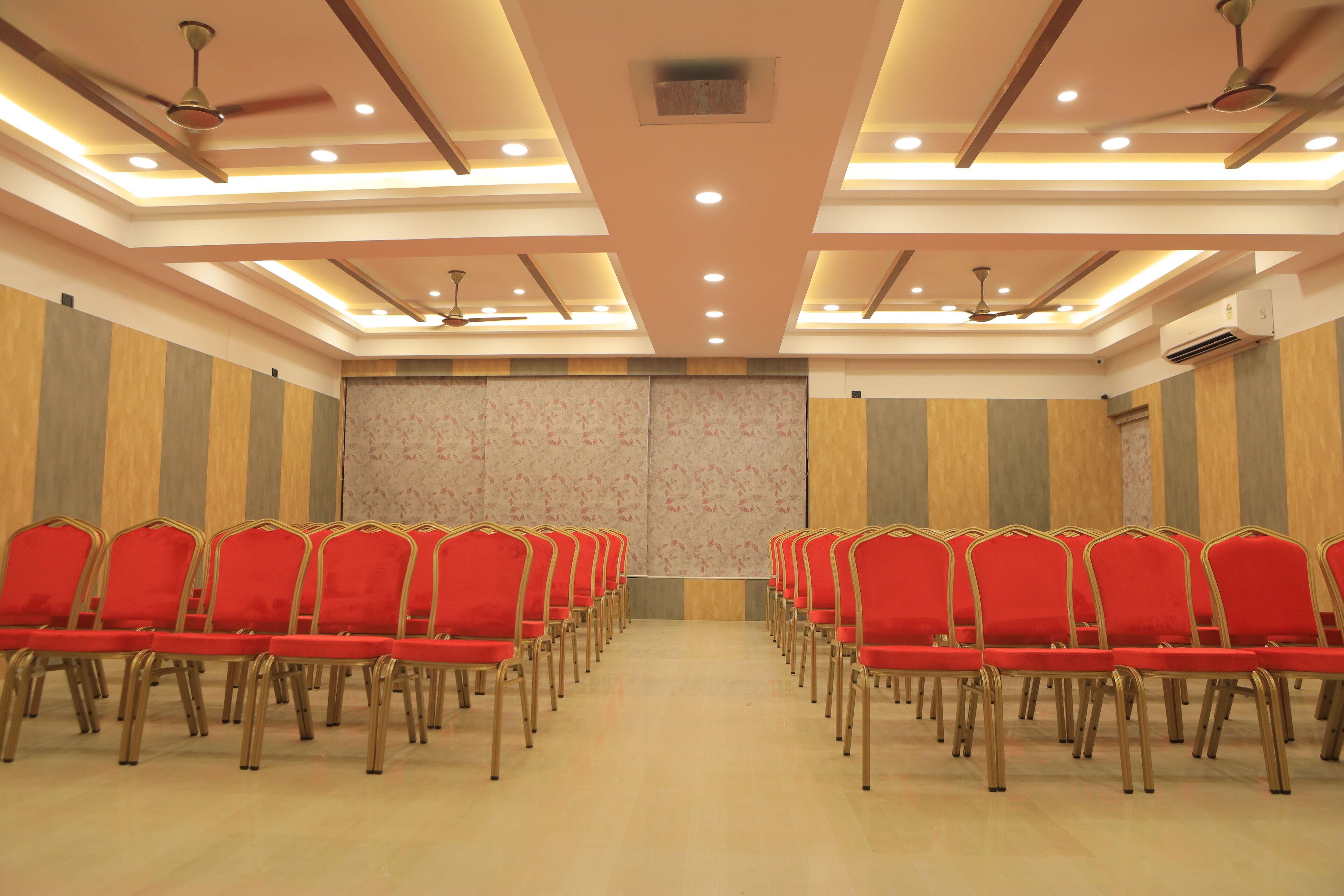 A conference room with rows of red chairs, ceiling fans, recessed lighting, and a wooden panel wall.