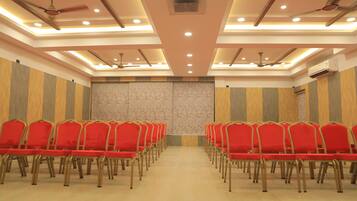 A conference room with rows of red chairs, ceiling fans, recessed lighting, and a wooden panel wall.