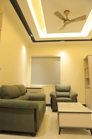 A room with a ceiling fan, two green sofas, a small table, and a cabinet. - Kansone Hotel And Banquets (Chennai)