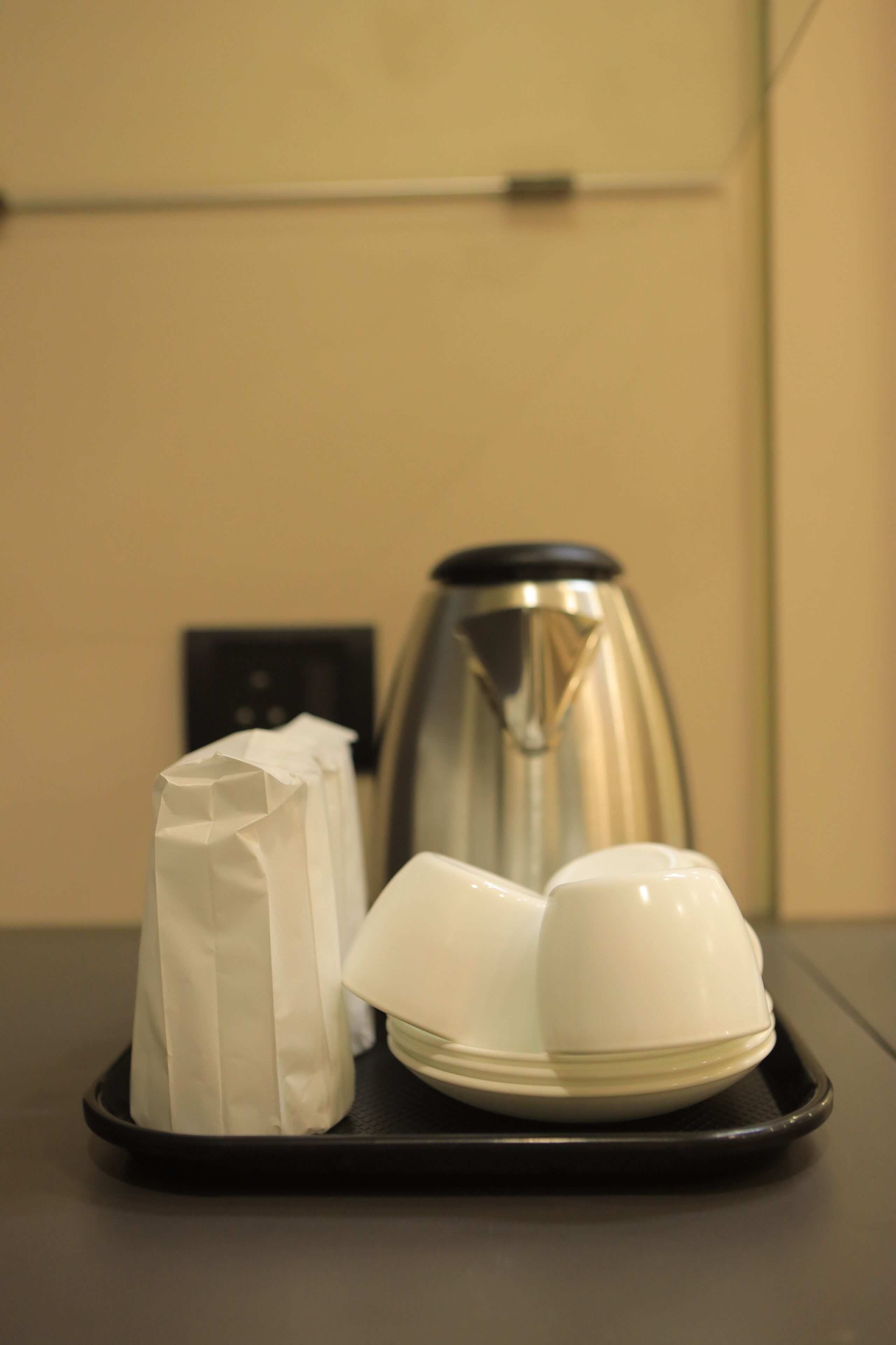A tray with a white bag, a white bowl, and a silver electric kettle on a table.
