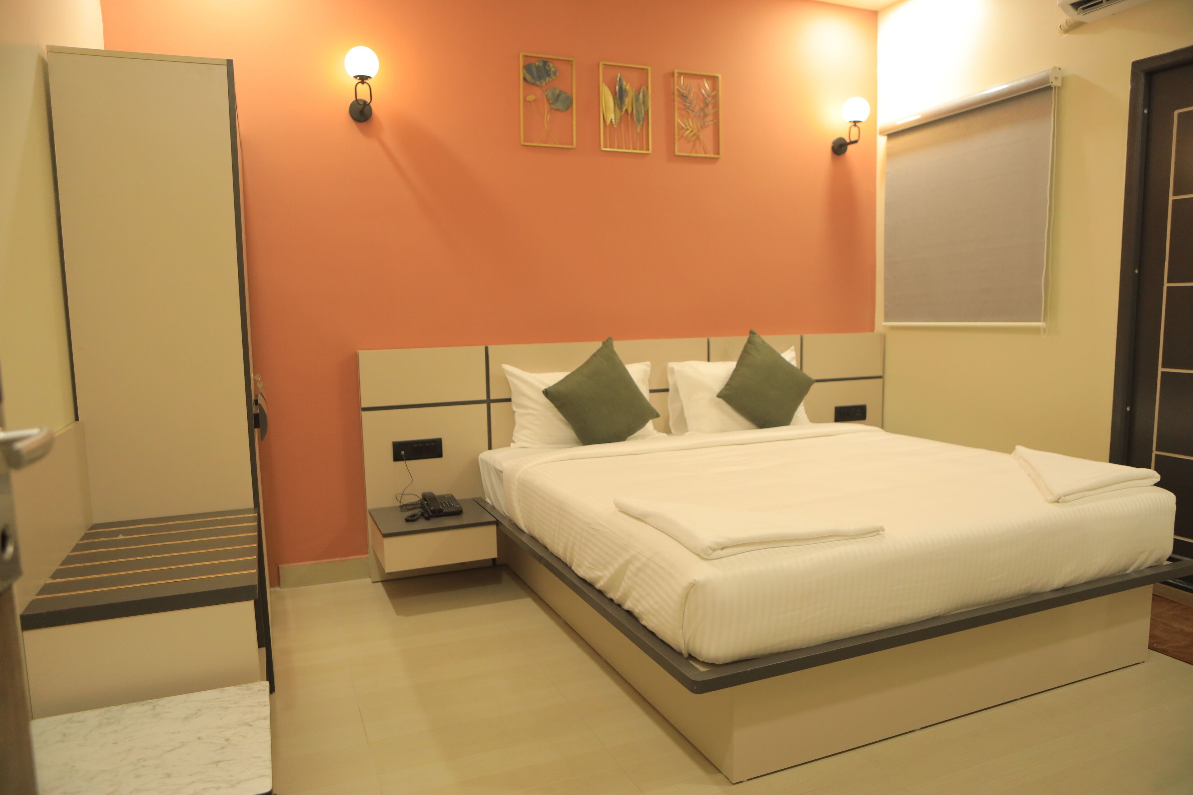 A bedroom with a bed, bedside tables, a nightstand, a door, and a wall-mounted light fixture.
