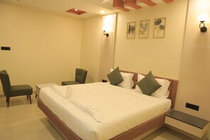 A hotel room with a large bed, a bedside table, a chair, and a small desk. - Kansone Hotel And Banquets (Chennai)