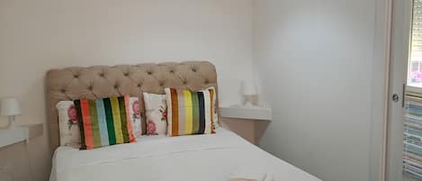 A bedroom with a tufted headboard, a white bedspread, and a green rug.