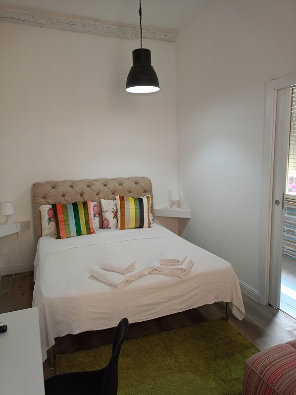 A bedroom with a tufted headboard, a white bedspread, and a green rug.