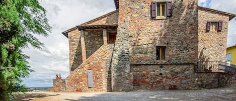 Un edificio de piedra con techo inclinado, una ventana pequeña con contraventanas y un camino de entrada de grava.